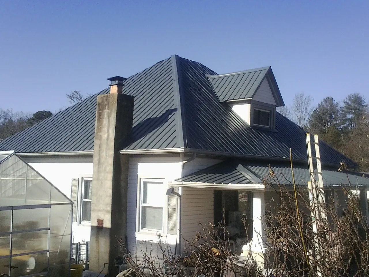 Dark blue standing seam metal roof on a white farmhouse with dormer — Slate & Tile Roof Repair by Roofing Brothers in Chappaqua