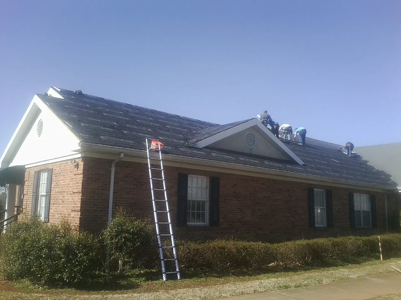 Crew tearing shingles off a brick ranch roof with a ladder set — Emergency Roof Repair work by our crew in Chappaqua