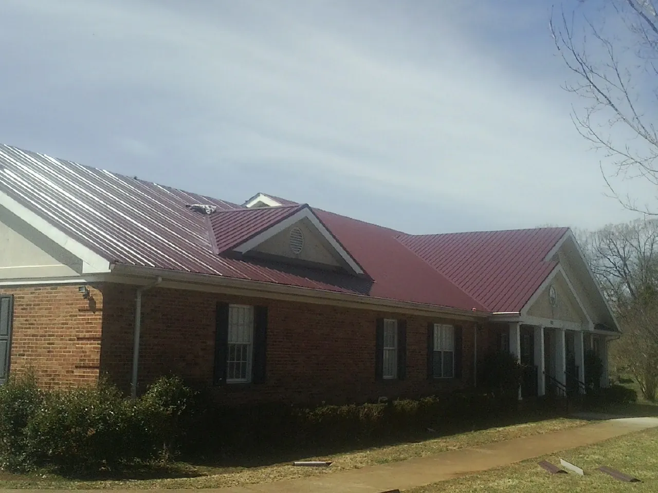 Red metal roof with gabled entries on a long brick building, from a Hail Damage Roof Repair job in Chappaqua