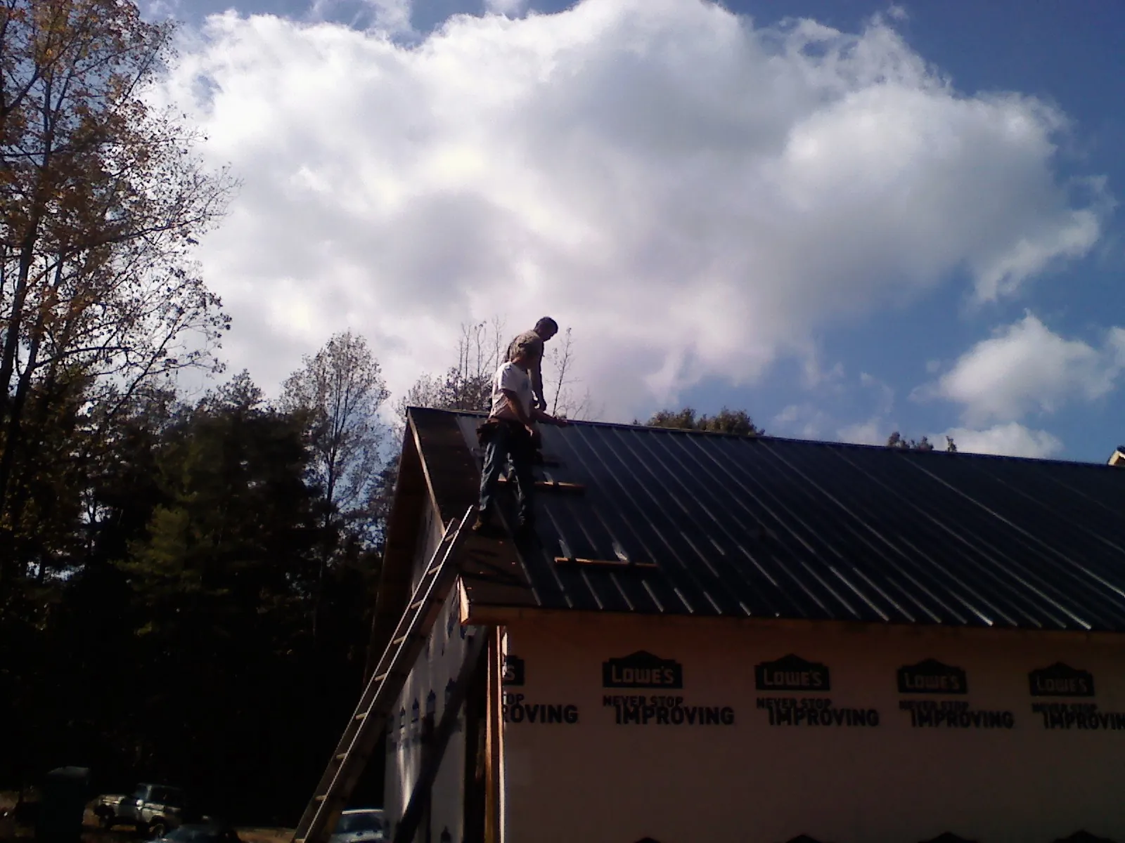 Roofer fastening dark metal panels high against a cloudy sky, from a Roof Inspection job in Chappaqua