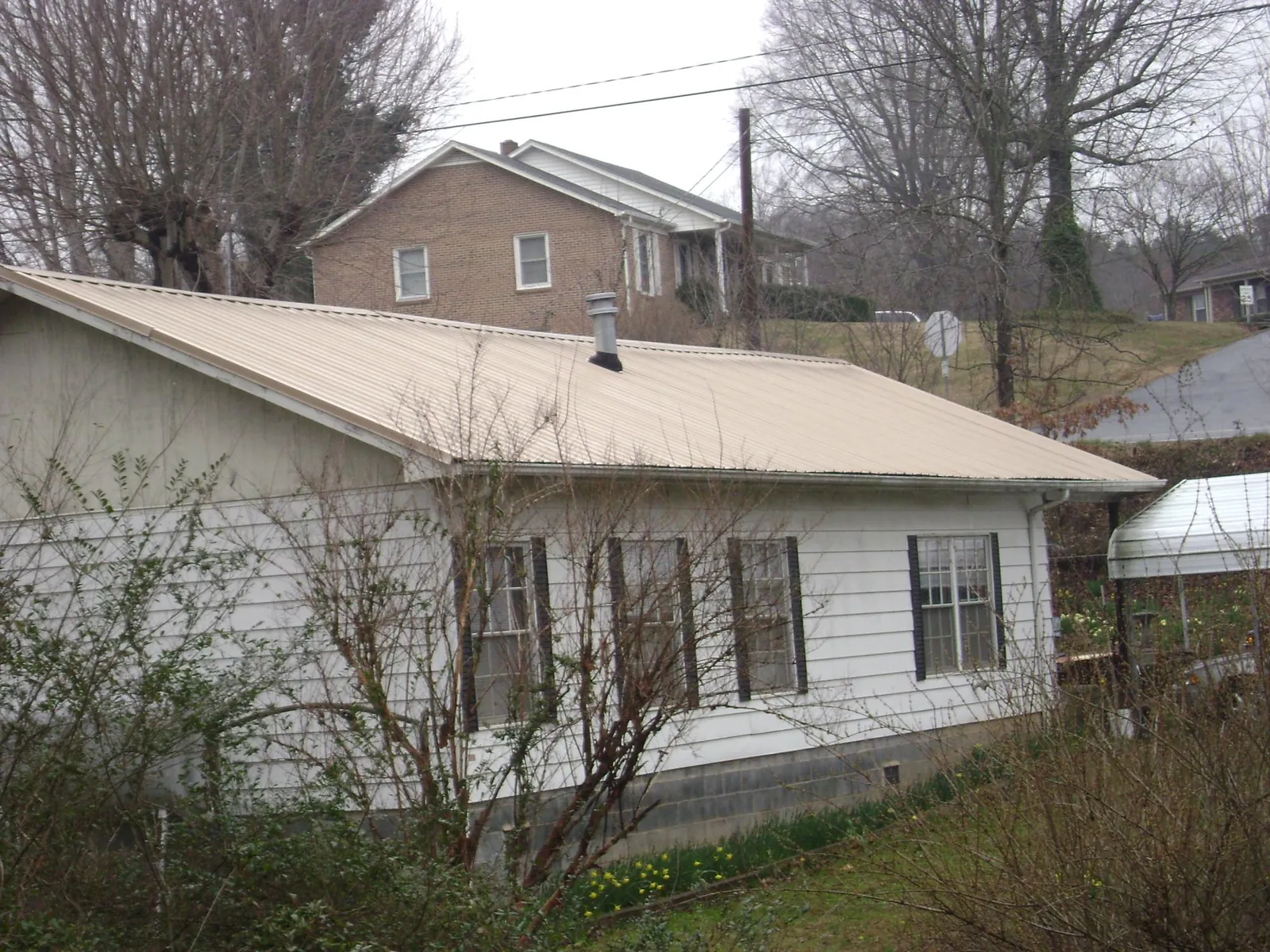 Tan metal roof on a white sided house set into a hillside — Commercial Roofing by Roofing Brothers in Chappaqua